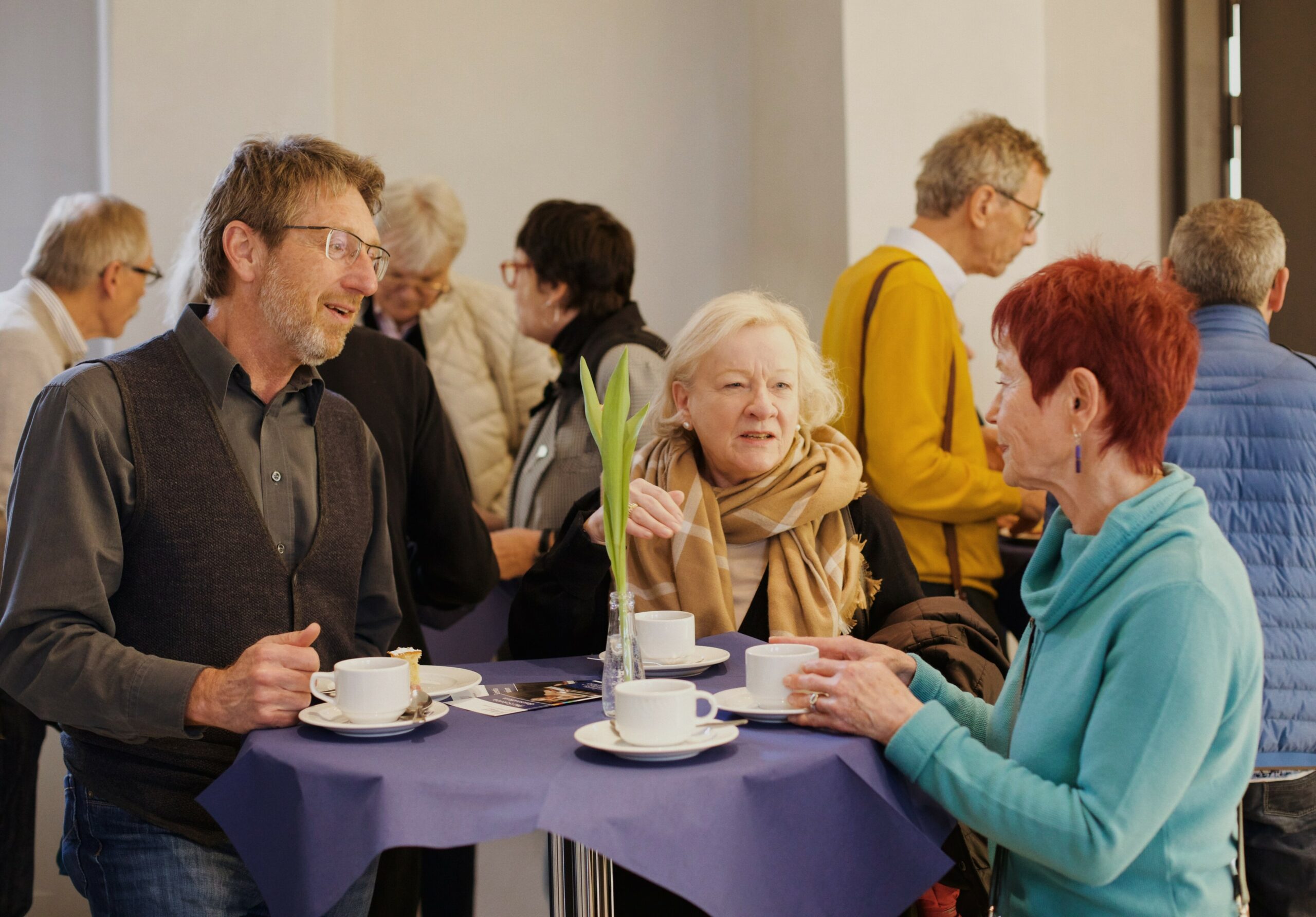 Drei Personen stehen an einem Stehtisch und unterhalten sich angeregt.